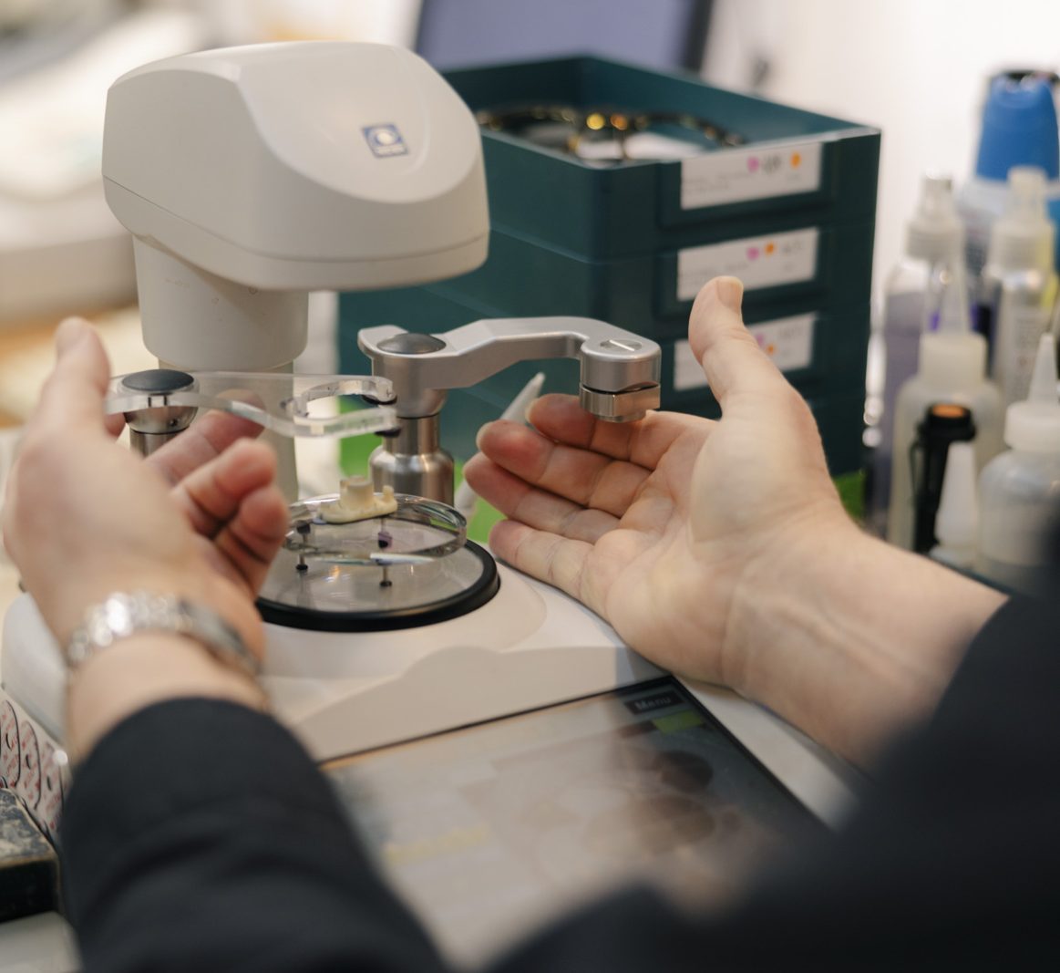 Hands finishing a lens on precision equipment.